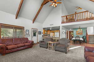 Carpeted living room featuring ceiling fan, high vaulted ceiling, stairs, and beamed ceiling