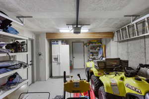 Garage with white refrigerator with ice dispenser and a garage door opener