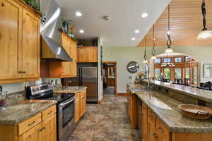 Kitchen with stainless steel appliances, range hood, a chandelier, a large island with sink, and recessed lighting
