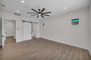 Unfurnished bedroom featuring a barn door, light wood finished floors, recessed lighting, and ceiling fan