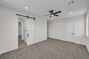Unfurnished bedroom featuring carpet flooring, a barn door, recessed lighting, and a ceiling fan
