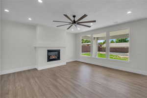 Unfurnished living room featuring recessed lighting, wood finished floors, a glass covered fireplace, and a ceiling fan