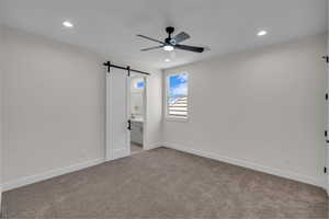 Unfurnished bedroom with a barn door, light carpet, recessed lighting, ensuite bathroom, and ceiling fan