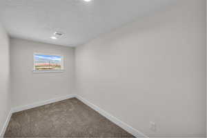 Empty room featuring dark carpet, a textured ceiling, and recessed lighting