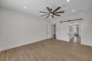 Empty room featuring a barn door, a ceiling fan, light wood finished floors, and recessed lighting