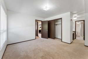 Unfurnished bedroom with light colored carpet, a closet, and ensuite bathroom