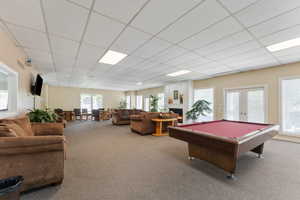 Playroom featuring carpet floors, a drop ceiling, billiards table, french doors, and a warm lit fireplace
