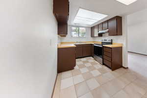 Kitchen featuring stainless steel range with electric cooktop, under cabinet range hood, butcher block countertops, and dark brown cabinets