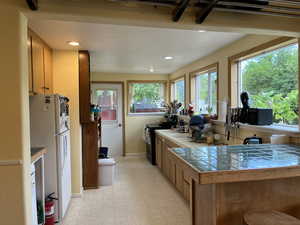 Kitchen featuring freestanding refrigerator, tile counters, range with electric stovetop, light floors, and recessed lighting