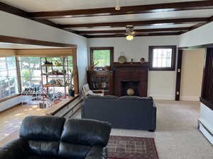 Carpeted living room featuring a baseboard heating unit, a ceiling fan, beamed ceiling, and a fireplace