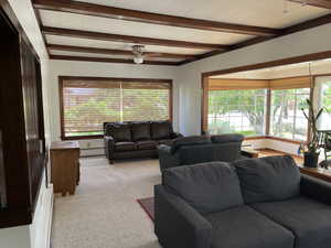Carpeted living room with baseboard heating, plenty of natural light, ceiling fan, and beam ceiling