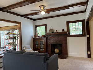 Living area featuring plenty of natural light, carpet flooring, a brick fireplace, a ceiling fan, and beamed ceiling