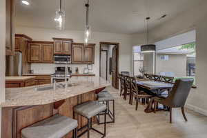 Kitchen with appliances with stainless steel finishes, a breakfast bar, decorative light fixtures, light stone counters, and recessed lighting