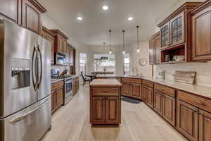 Kitchen with stainless steel appliances, a peninsula, recessed lighting, pendant lighting, and glass insert cabinets