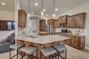 Kitchen featuring appliances with stainless steel finishes, a peninsula, light wood finished floors, a kitchen breakfast bar, and arched walkways