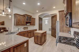 Kitchen with appliances with stainless steel finishes, arched walkways, light wood finished floors, light stone counters, and open shelves
