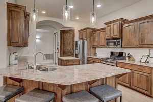 Kitchen featuring appliances with stainless steel finishes, a peninsula, a breakfast bar, light stone counters, and recessed lighting