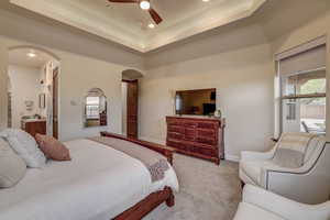 Carpeted bedroom with arched walkways, recessed lighting, ceiling fan, a tray ceiling, and connected bathroom