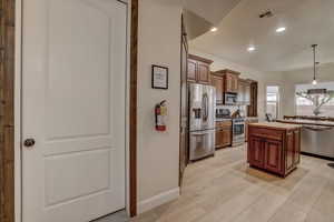 Kitchen featuring appliances with stainless steel finishes, a center island, decorative light fixtures, butcher block counters, and light wood-style floors