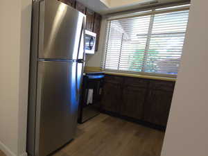 Kitchen with appliances with stainless steel finishes, dark brown cabinetry, dark wood-style floors, and light countertops