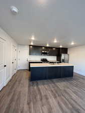 Five plex  Kitchen featuring appliances with stainless steel finishes, light countertops, dark wood-style floors, an island with sink, and a textured ceiling