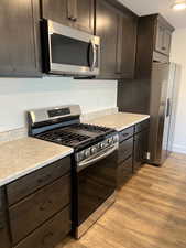 Five plex  Kitchen featuring appliances with stainless steel finishes, light wood-style flooring, dark brown cabinetry, and light countertops