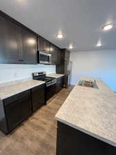 Kitchen with appliances with stainless steel finishes, wood finished floors, a textured ceiling, light countertops, and recessed lighting