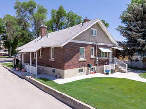 Back of house featuring a chimney, brick siding, and a yard