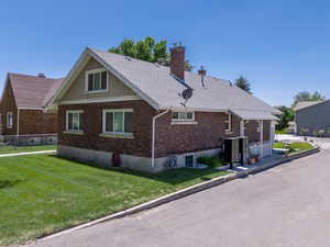 View of property Front exterior with a side lower entrance chimney, brick siding, a lawn, and a shingled roof