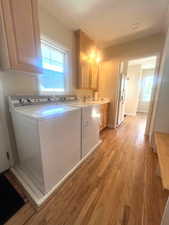Laundry area featuring separate washer and dryer, cabinet space, and light wood-style floors