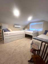 Carpeted bedroom with a wall mounted air conditioner and lofted ceiling