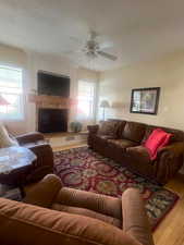 Living area with wood finished floors, plenty of natural light, a fireplace, and ceiling fan