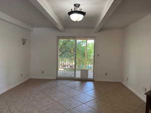 Empty room with beam ceiling and light tile patterned floors