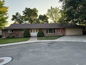 Ranch-style house with an attached garage, concrete driveway, brick siding, and a front lawn