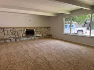 Unfurnished living room featuring beamed ceiling, carpet flooring, plenty of natural light, a stone fireplace, and a textured ceiling