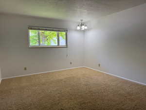 Spare room with a chandelier, a textured ceiling, and carpet floors