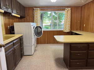 Laundry room with wood walls, washer and clothes dryer, cabinet space, and a textured ceiling