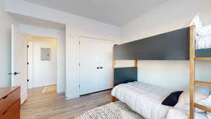 Bedroom featuring electric panel, light wood-type flooring, and a closet