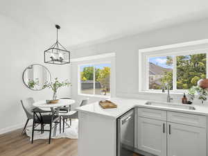 Kitchen with stainless steel dishwasher, light countertops, light wood-style flooring, a chandelier, and decorative light fixtures
