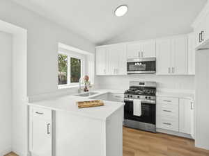 Kitchen featuring appliances with stainless steel finishes, a peninsula, white cabinetry, light countertops, and light wood-style flooring