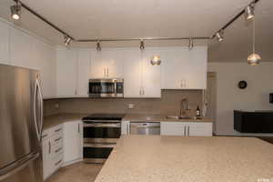 Kitchen with appliances with stainless steel finishes, backsplash, white cabinets