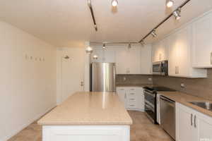 Kitchen with stainless steel appliances, a kitchen island, decorative backsplash, white cabinetry, and light stone countertops