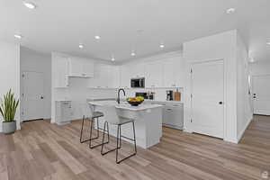 Kitchen with a breakfast bar, white cabinetry, a center island with sink, recessed lighting, and light wood-style flooring