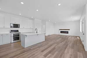 Kitchen featuring stainless steel appliances, white cabinetry, recessed lighting, open floor plan, and a glass covered fireplace
