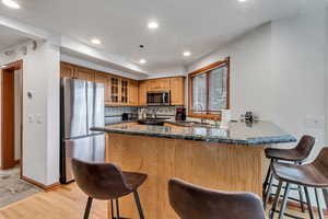 Kitchen with stainless steel appliances, light wood-type flooring, glass insert cabinets, a peninsula, and a kitchen bar