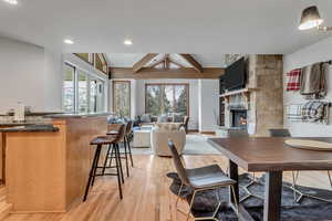 Dining area featuring light wood finished floors, a stone fireplace, beam ceiling, and recessed lighting