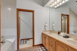 Bathroom featuring double vanity, a shower stall, a bath, vaulted ceiling, and wood finished floors