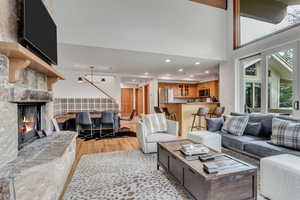 Living area featuring light wood-style flooring, recessed lighting, a stone fireplace, and a high ceiling