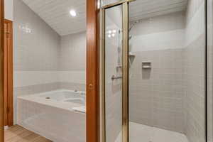 Bathroom featuring a garden tub, a shower stall, wood finished floors, recessed lighting, and vaulted ceiling
