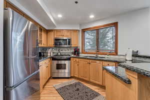 Kitchen with stainless steel appliances, light wood finished floors, dark stone countertops, tasteful backsplash, and recessed lighting
